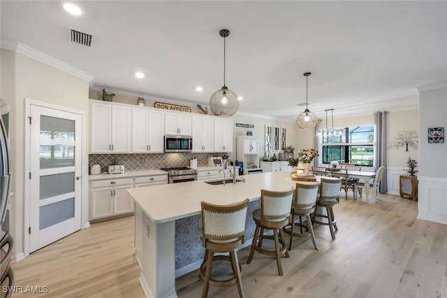 17476 Ashcomb Way, Estero, FL 33928 - kitchen with appliances with stainless steel finishes, crown molding, white cabinets, a kitchen island with sink, and light countertops
