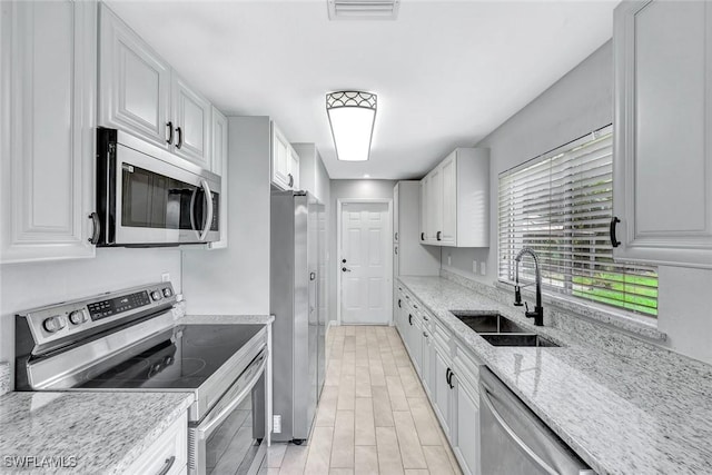 13820 2nd St, Fort Myers, FL 33905 - kitchen featuring stainless steel appliances, a sink, white cabinetry, light stone counters, and light wood-type flooring