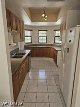 718 Jefferson Ave, Lehigh Acres, FL 33936 - kitchen featuring freestanding refrigerator, a tray ceiling, brown cabinets, light tile patterned flooring, and a sink