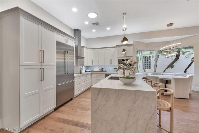 917 Tierra Lago Way, Naples, FL 34119 - kitchen with appliances with stainless steel finishes, wall chimney range hood, a breakfast bar area, a sink, and light stone counters