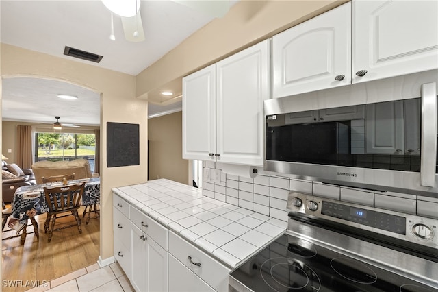 909 SE 46th Ln Unit 104, Cape Coral, FL 33904 - kitchen with appliances with stainless steel finishes, tile countertops, white cabinetry, backsplash, and arched walkways