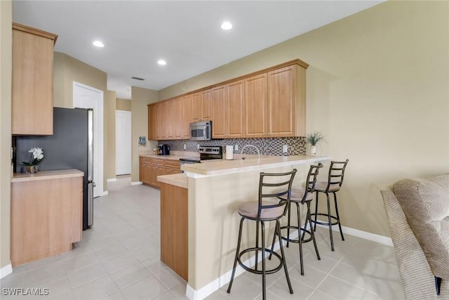 3032 Lake Manatee Ct, Cape Coral, FL 33909 - kitchen with stainless steel appliances, a peninsula, a breakfast bar area, backsplash, and baseboards