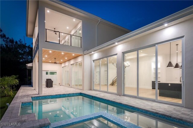 2854 Coach House Way, Naples, FL 34105 - back of house at twilight with stucco siding, a patio area, a balcony, ceiling fan, and a pool with connected hot tub