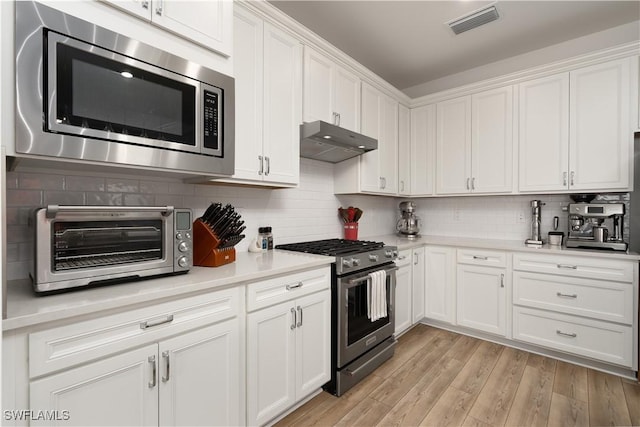 42530 Atlas Dr, Punta Gorda, FL 33982 - kitchen featuring appliances with stainless steel finishes, under cabinet range hood, white cabinets, light countertops, and tasteful backsplash