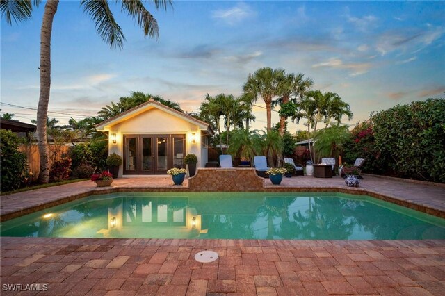 10340 Vanderbilt Dr, Naples, FL 34108 - pool at dusk featuring french doors, a patio area, a storage structure, and an outbuilding