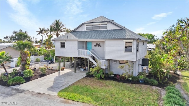 3627 Clipper Ln, Saint James City, FL 33956 - raised beach house with a shingled roof, stairway, concrete driveway, a carport, and a front lawn