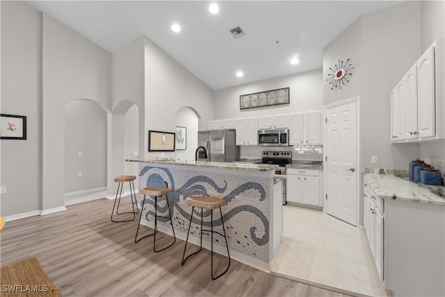 14769 Calusa Palms Dr Unit 203, Fort Myers, FL 33919 - kitchen featuring appliances with stainless steel finishes, arched walkways, a kitchen breakfast bar, white cabinetry, and a towering ceiling