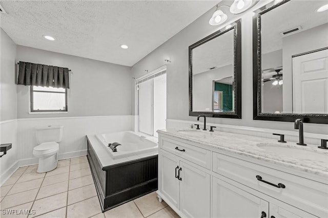 1311 SE 11th St, Cape Coral, FL 33990 - bathroom with wainscoting, double vanity, a textured ceiling, a bath, and tile patterned floors