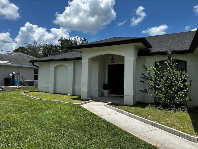 1839 Jovita Ave, Lehigh Acres, FL 33972 - view of exterior entry with a shingled roof, a yard, stucco siding, and central air condition unit