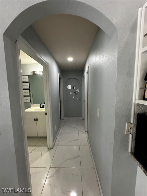 1839 Jovita Ave, Lehigh Acres, FL 33972 - hallway with light marble finish floors, arched walkways, baseboards, and a sink