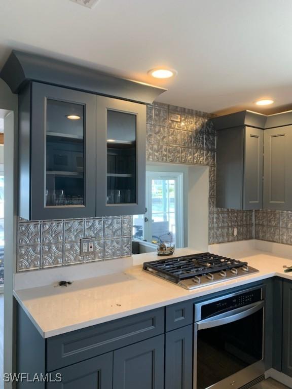 2685 Geary St, Matlacha, FL 33993 - kitchen featuring stainless steel appliances, gray cabinets, backsplash, light countertops, and glass insert cabinets