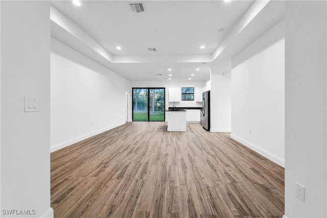 902 Magnolia Ave, Lehigh Acres, FL 33972 - unfurnished living room featuring light wood-style flooring, recessed lighting, a tray ceiling, baseboards, and a sink