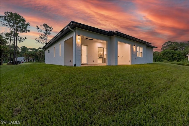 3762 32nd Ave SE, Naples, FL 34117 - back of property at dusk featuring a lawn, stucco siding, and a ceiling fan