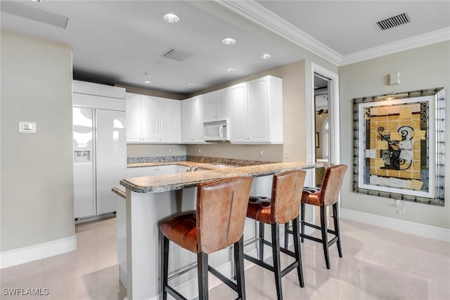 900 5th Ave S Unit 302, Naples, FL 34102 - kitchen with white microwave, paneled refrigerator, light stone countertops, a kitchen breakfast bar, and crown molding