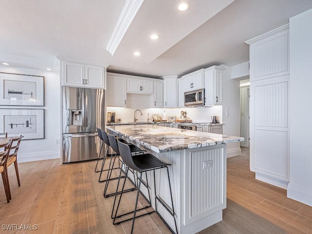 9375 Gulf Shore Dr Unit 601, Naples, FL 34108 - kitchen with stainless steel appliances, light stone counters, white cabinetry, light wood-type flooring, and a breakfast bar