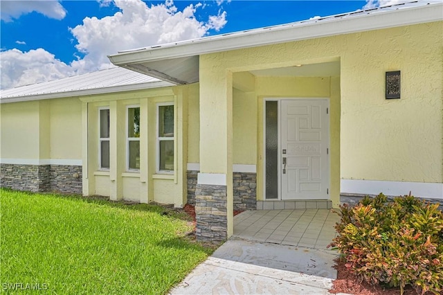 14938 Randolph Dr, Fort Myers, FL 33905 - view of exterior entry featuring stone siding, stucco siding, metal roof, and a lawn