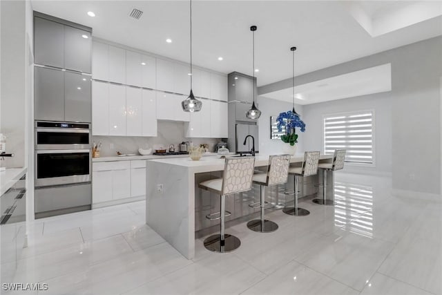 2909 2nd Ave NE, Naples, FL 34120 - kitchen with modern cabinets, double oven, white cabinets, a kitchen breakfast bar, and a spacious island
