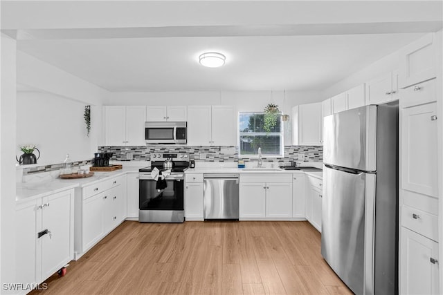 3303 6th St SW, Lehigh Acres, FL 33976 - kitchen featuring stainless steel appliances, a sink, light wood-style flooring, tasteful backsplash, and white cabinetry