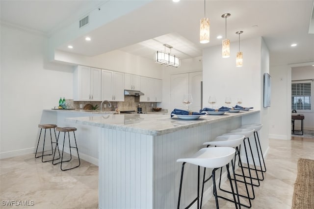 560 El Camino Real Unit 1304, Naples, FL 34119 - kitchen with under cabinet range hood, a peninsula, white cabinets, a breakfast bar, and recessed lighting