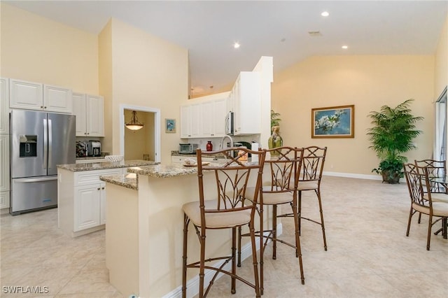 16121 Sand Ridge Ct, Fort Myers, FL 33908 - kitchen with stainless steel appliances, a peninsula, light stone counters, high vaulted ceiling, and white cabinetry