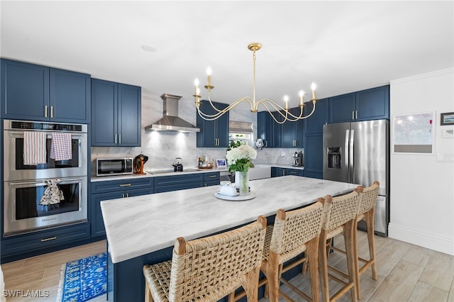 1549 Sandpiper St Unit 39, Naples, FL 34102 - kitchen featuring blue cabinetry, wall chimney exhaust hood, stainless steel appliances, light wood-style flooring, and backsplash
