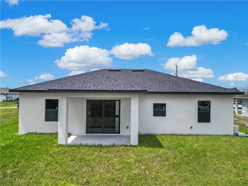 2811 27th St SW, Lehigh Acres, FL 33976 - back of property with roof with shingles, stucco siding, a yard, and a patio