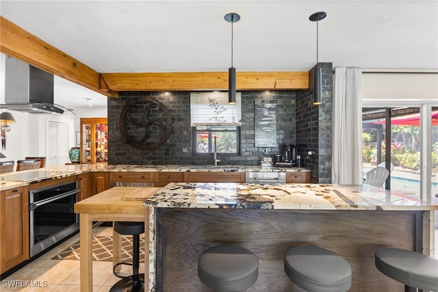 5631 Shaddelee Ln W, Fort Myers, FL 33919 - kitchen featuring stainless steel oven, wall chimney range hood, black electric stovetop, a breakfast bar, and brown cabinets