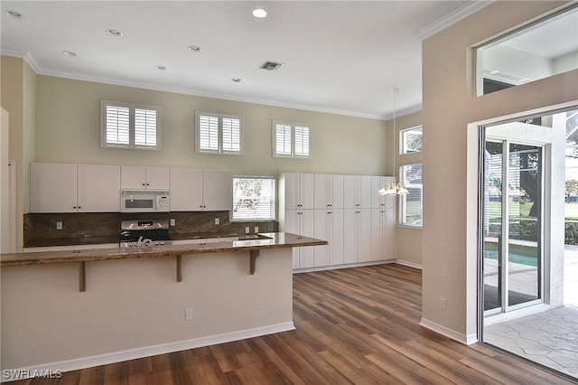 19741 Vintage Trace Cir, Estero, FL 33967 - kitchen featuring white microwave, stove, crown molding, a breakfast bar area, and dark wood-style flooring