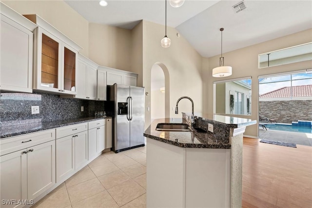 1435 Vintage Ln, Naples, FL 34104 - kitchen featuring stainless steel refrigerator with ice dispenser, white cabinets, tasteful backsplash, dark stone countertops, and a center island with sink