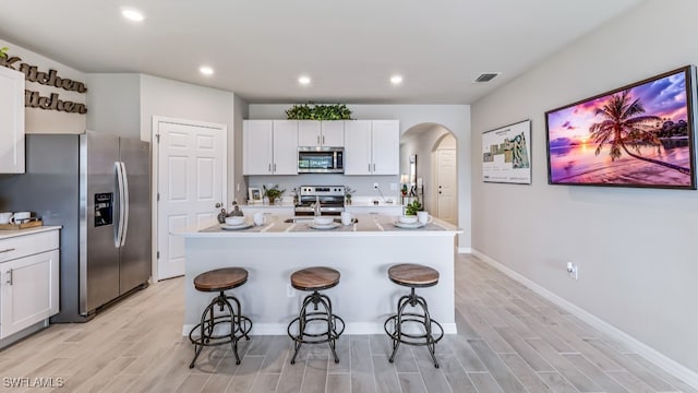 1255 Brumfield Xing, Fort Myers, FL 33905 - kitchen with stainless steel appliances, arched walkways, light wood-style floors, a kitchen breakfast bar, and white cabinets