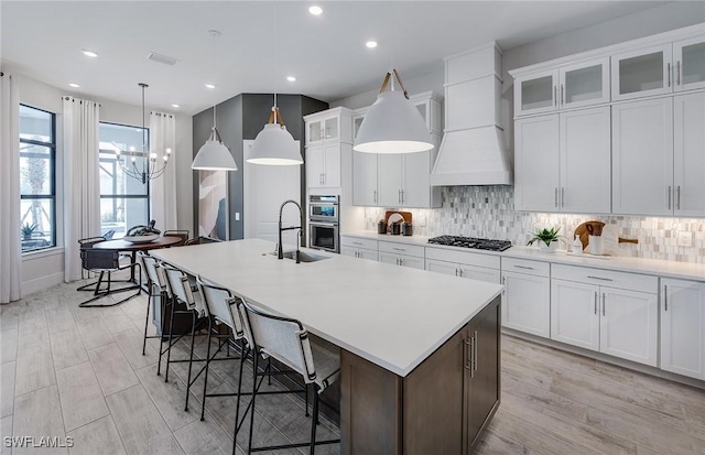 1825 Verada Ct, Naples, FL 34120 - kitchen featuring premium range hood, double oven, a kitchen island with sink, gas stovetop, and light wood-style floors