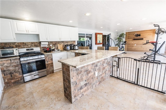 4924 20th Pl SW, Naples, FL 34116 - kitchen with stainless steel gas range oven, a peninsula, recessed lighting, white cabinetry, and decorative backsplash