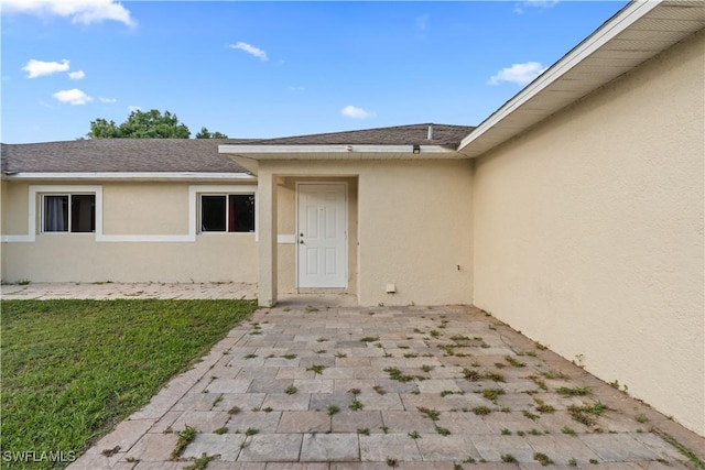 209 Meadow Rd, Lehigh Acres, FL 33973 - doorway to property featuring stucco siding, roof with shingles, a yard, and a patio