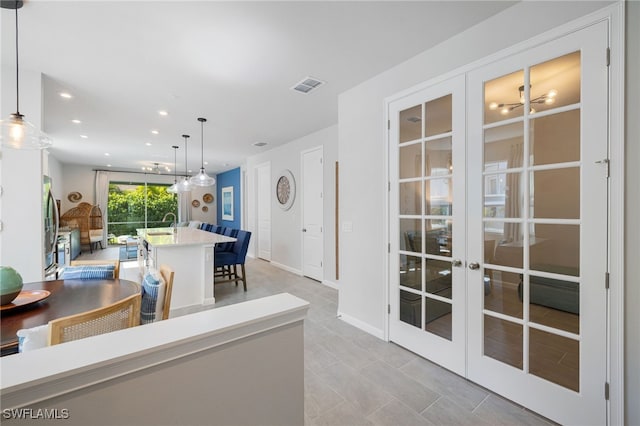 4665 Arboretum Cir Unit 101, Naples, FL 34112 - kitchen featuring french doors, a center island with sink, recessed lighting, light countertops, and decorative light fixtures