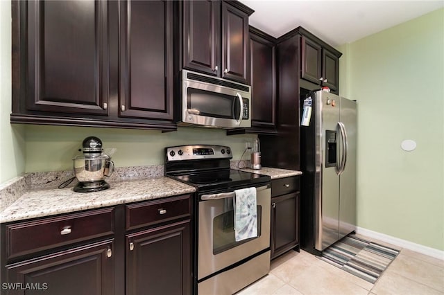 8570 Evernia Ct Unit 101, Estero, FL 34135 - kitchen with appliances with stainless steel finishes, dark brown cabinets, baseboards, light tile patterned floors, and light stone counters