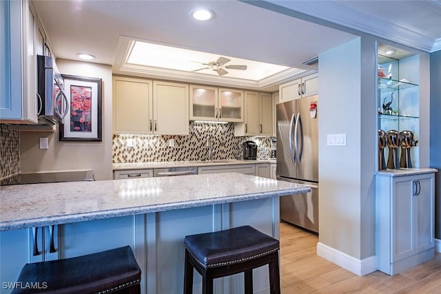 3443 Gulf Shore Blvd N Unit 409, Naples, FL 34103 - kitchen featuring appliances with stainless steel finishes, a kitchen bar, light wood-style floors, light stone countertops, and tasteful backsplash