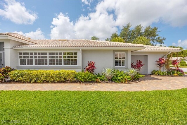 13461 Bridgeford Ave, Bonita Springs, FL 34135 - view of property exterior with stucco siding, a garage, a tiled roof, and a lawn