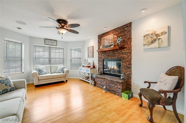 20433 Fern Cir, North Fort Myers, FL 33917 - living room featuring healthy amount of natural light, a stone fireplace, ceiling fan, and light wood-style flooring