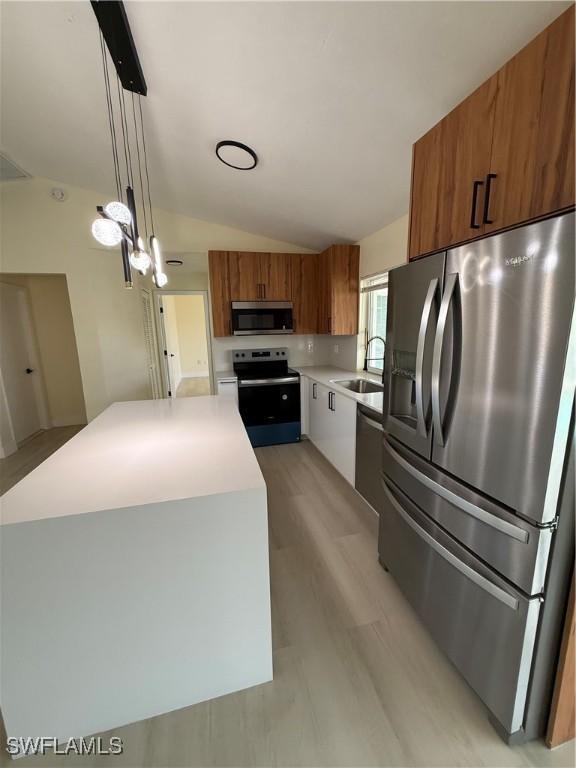 2803 E 5th St, Lehigh Acres, FL 33972 - kitchen with stainless steel appliances, brown cabinets, vaulted ceiling, a kitchen island, and light countertops