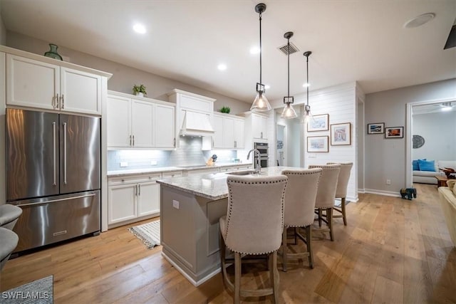 14372 Neptune Ave, Naples, FL 34114 - kitchen with appliances with stainless steel finishes, custom exhaust hood, an island with sink, backsplash, and white cabinetry