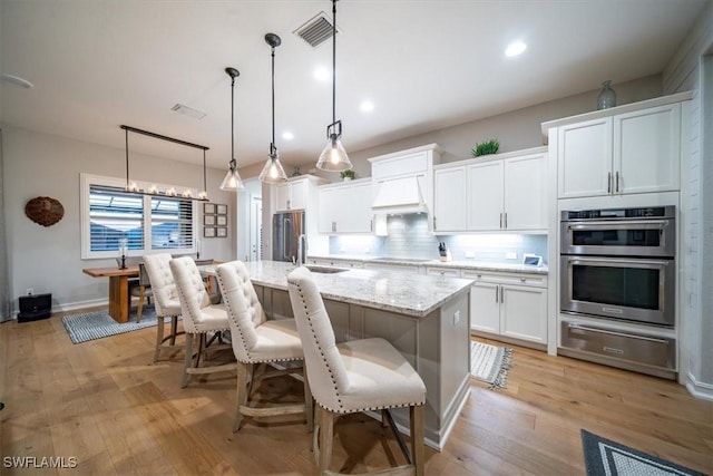 14372 Neptune Ave, Naples, FL 34114 - kitchen featuring a warming drawer, appliances with stainless steel finishes, premium range hood, a center island with sink, and tasteful backsplash