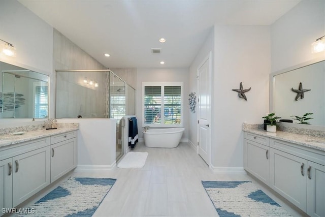 14372 Neptune Ave, Naples, FL 34114 - full bathroom featuring two vanities, a shower stall, a freestanding tub, recessed lighting, and baseboards