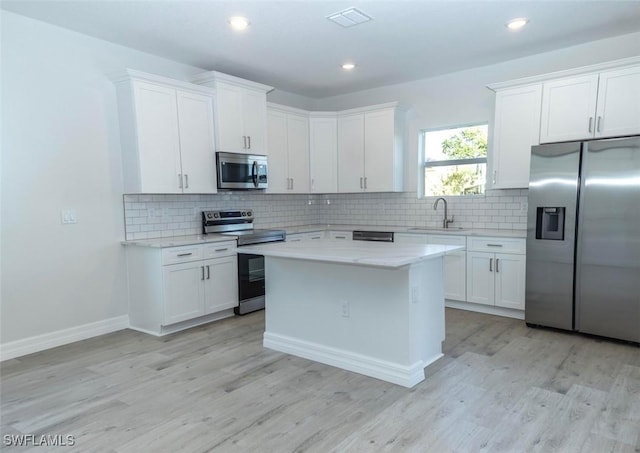 17211 Nile Ct, Punta Gorda, FL 33955 - kitchen featuring stainless steel appliances, white cabinetry, light wood-style flooring, backsplash, and a center island