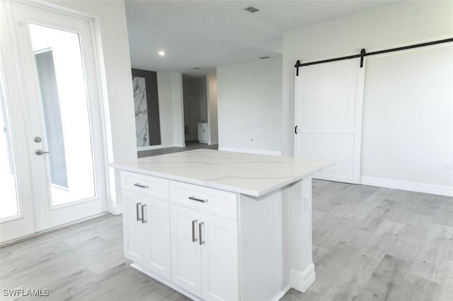 17211 Nile Ct, Punta Gorda, FL 33955 - kitchen with light stone countertops, a barn door, white cabinets, light wood-type flooring, and recessed lighting