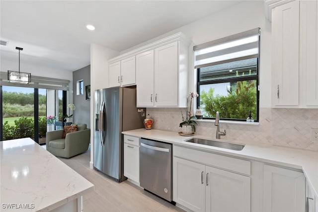 5596 Celebration Dr, Ave Maria, FL 34142 - kitchen with stainless steel appliances, a sink, backsplash, white cabinets, and decorative light fixtures