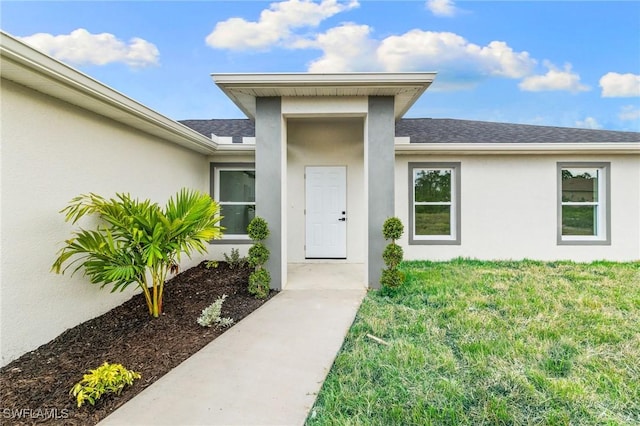 955 Plantation Rd, Lehigh Acres, FL 33974 - view of exterior entry with roof with shingles, stucco siding, and a lawn