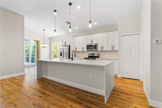 3519 Heron Cove Ct, Bonita Springs, FL 34134 - kitchen featuring appliances with stainless steel finishes, a kitchen island with sink, light countertops, light wood-style flooring, and baseboards
