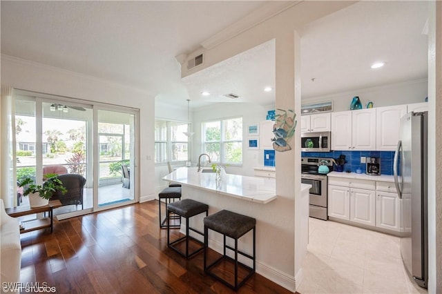 4610 Hawks Nest Dr Unit A104, Naples, FL 34114 - kitchen with appliances with stainless steel finishes, white cabinets, a breakfast bar area, tasteful backsplash, and ornamental molding
