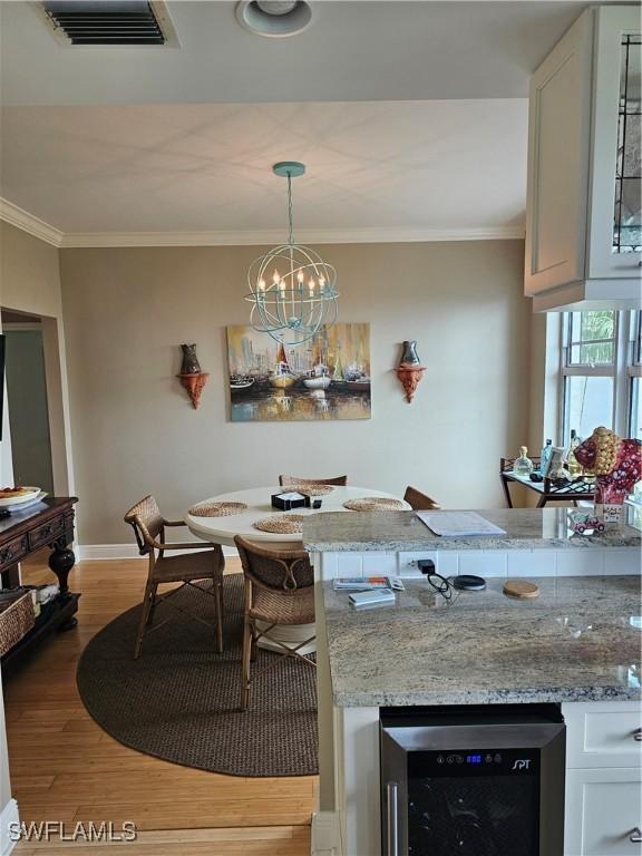 430 Cove Tower Dr Unit 501, Naples, FL 34110 - dining area with beverage cooler, light wood-style floors, ornamental molding, baseboards, and a chandelier