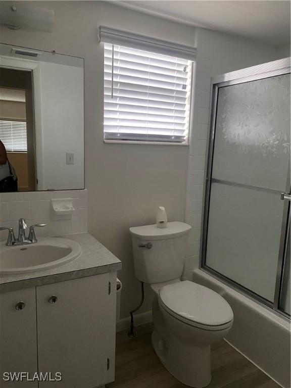 1516 Tropic Ter Unit 1516, North Fort Myers, FL 33903 - bathroom featuring vanity, toilet, combined bath / shower with glass door, wood finished floors, and plenty of natural light